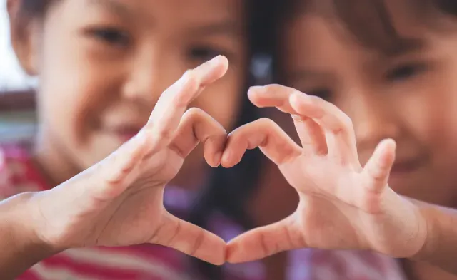 Two cute asian child girls making heart shape with hands together